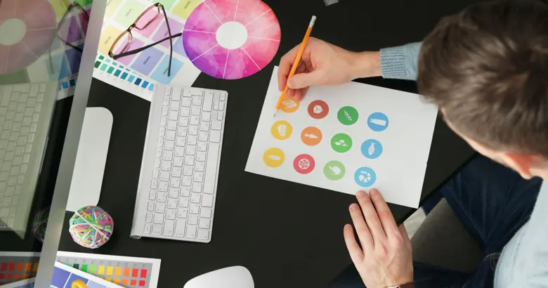 Designer working on logo concepts with colorful icons and design tools on a desk