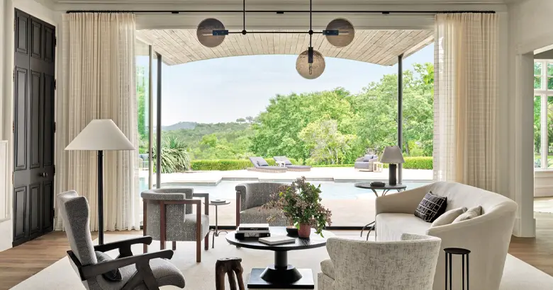 A naturally-lit living room with sofas and single seating options overlooking the swimming pool