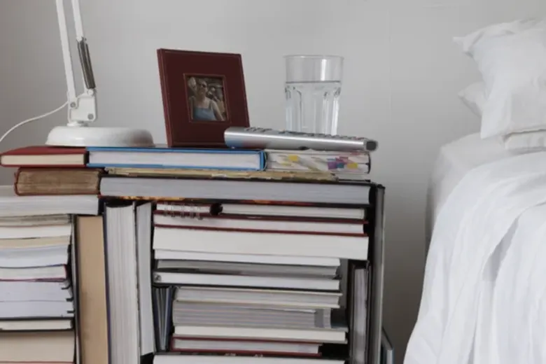 Side table made from piles of books next to the bed in a small bedroom.
Side table made from piles of books next to the bed in a small bedroom.