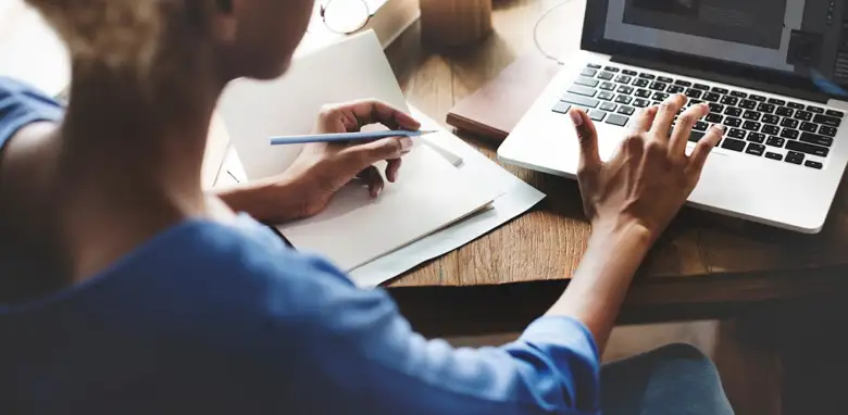 UX researcher working at a desk, reviewing and evaluating upcoming design thinking tools on a computer with a notepad.