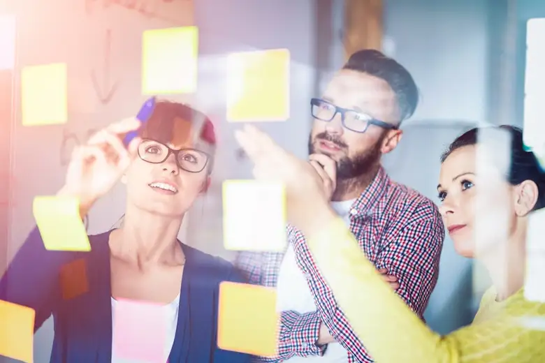Middle-aged professional explaining design thinking for innovation using a transparent glass board and sticky notes.
