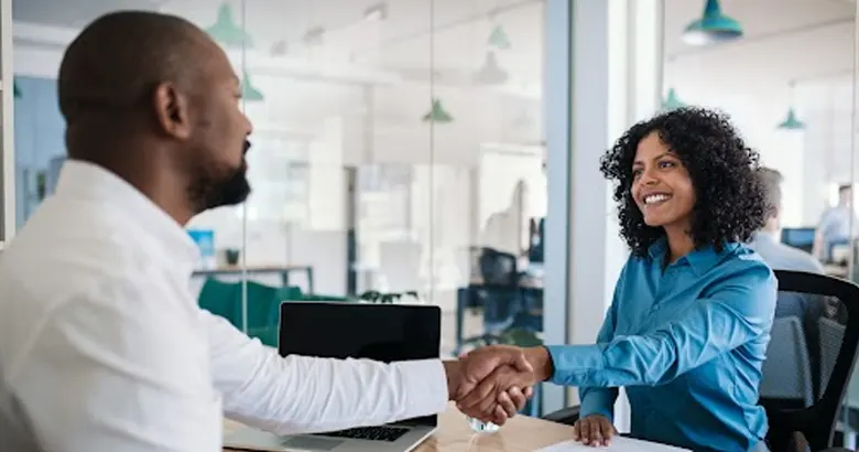 Middle-aged man congratulates young woman with a handshake during an interview for the UX designer candidate selection.
