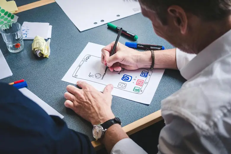 Middle-aged men using pen and paper to create wireframes by following design thinking process