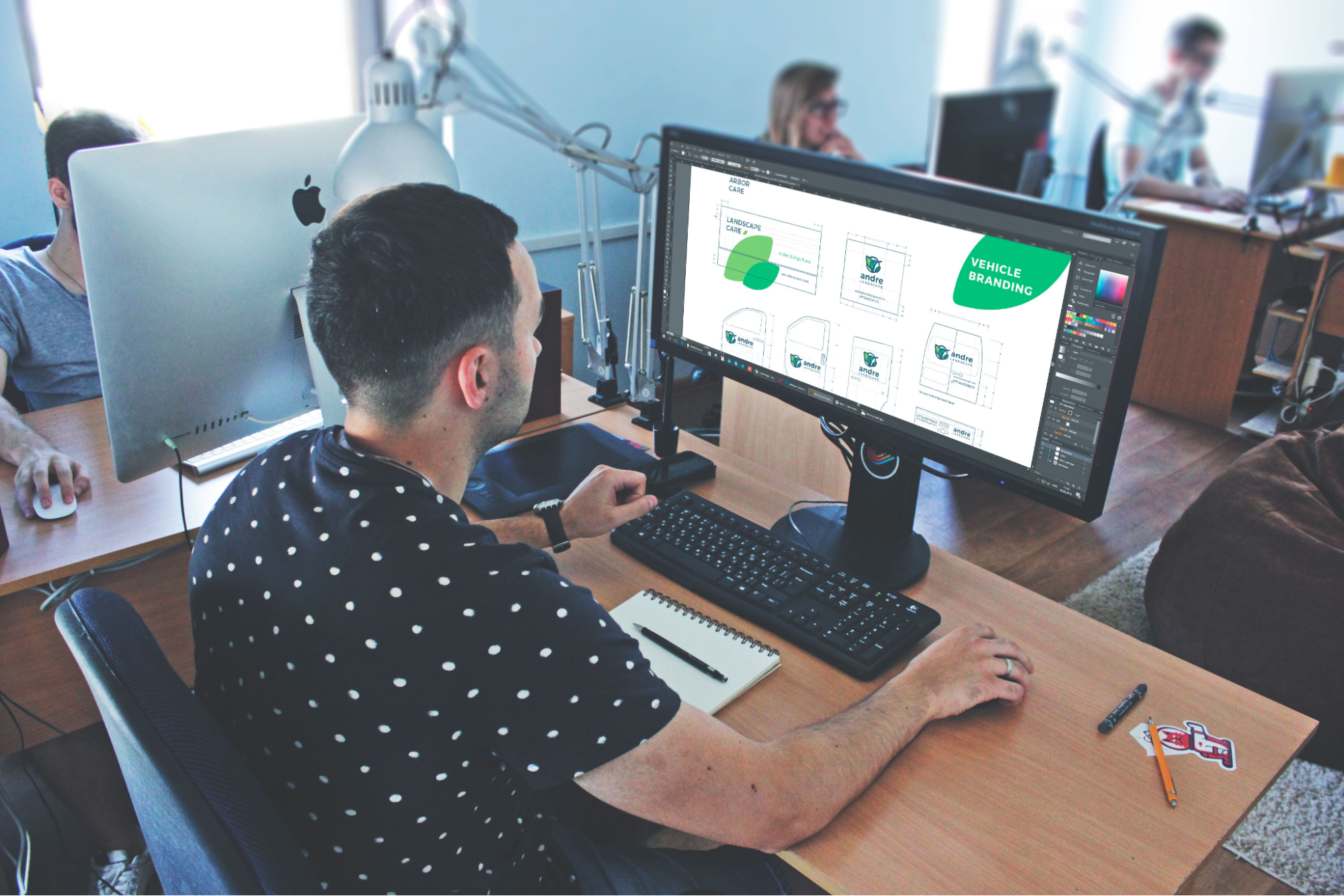 A man in an office, working on branding design tasks at his computer.