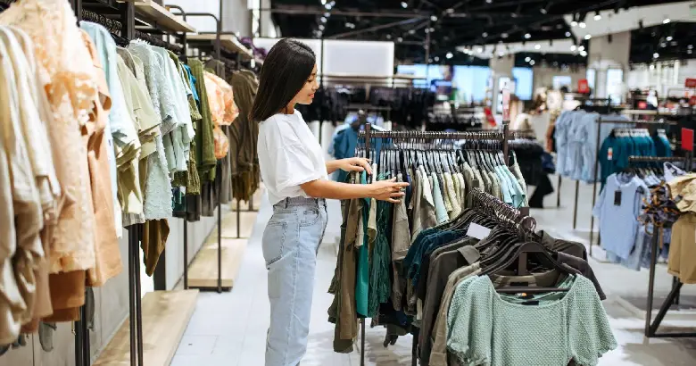 A visual merchandiser inspects dresses on a hanger in a store.