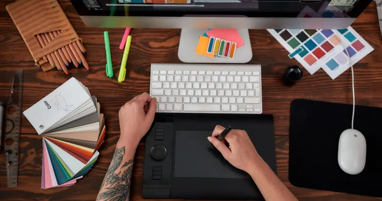 Graphic designer's workspace with computer and color palettes.